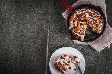 british english traditional pastries. cookies pie cranberry scones with orange peel, with sweet white glaze, in a frying pan and on a plate. black stone table, copy space top view