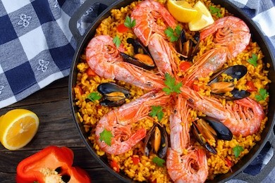 close-up of delicious seafood valencia paella with king prawns, mussels on savory creamy saffron rice with spices and lemon wedges in pan, on wooden table, view from above