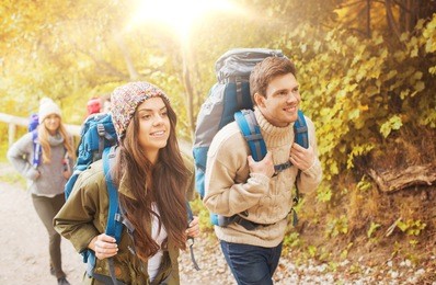 adventure, travel, tourism, hike and people concept - group of smiling friends walking with backpacks in autumn forest