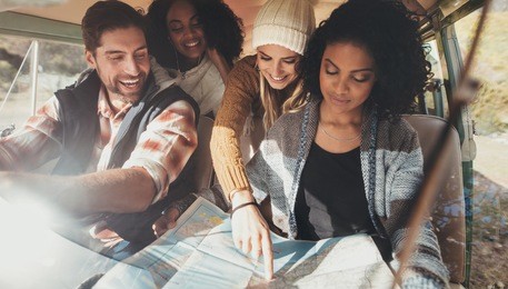 friends on roadtrip reading map for directions. group of man and women travelling together in van.