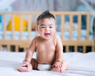 asian new born baby sit and smile on a white bed in bed room