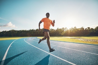 fit and focused young african male athlete running alone along a race track while out training on a sunny day