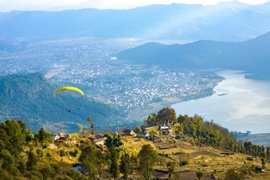 high angle aerial view of paraglider descending onto pokhara and phewa lake seen from sarangkot, nepal