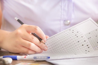 soft focus.high school or university student holding pencil writing on paper answer sheet.sitting on lecture chair taking final exam attending in examination room or classroom.student in uniform.