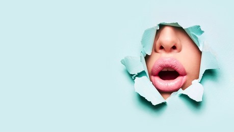 beautiful plump bright lips of pink color peep into the slit of colored paper.make-up, makeup, advertising, facial, boutique, smooth skin, emotions, surprise.