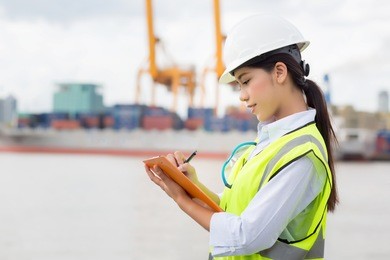 asian woman engineer use check sheet for control loading containers box from cargo freight ship for import and export