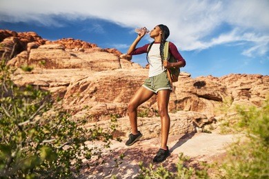 athletic african american female hiker drinking from water bottle at red rock canyon        
