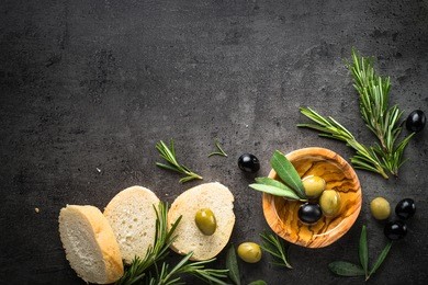black and green olives olive oil and bread on black slate background. top view  with space for text.