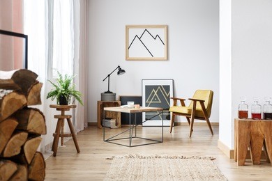 modern designed interior of cozy white living room with coffee table, armchair, posters and firewood