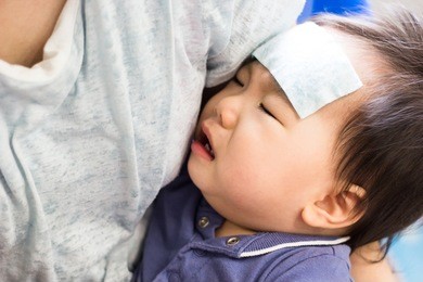 mother is holding a sick little baby. the baby has a high fever and he is crying while his mother put cool gel on his head.