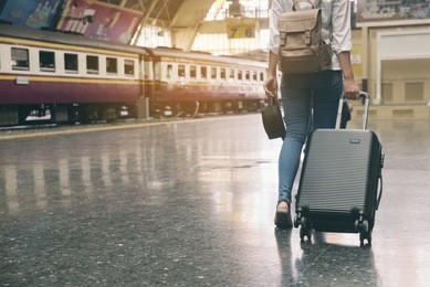at train station,young tourist girl walking,dragging luggage suitcase and searching right direction.asian backpacker waiting train and planning happy holiday vacation.travel concept.