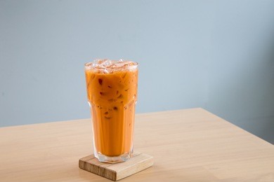 a glass of ice milk tea, fresh and sweet dessert on a wooden saucer 