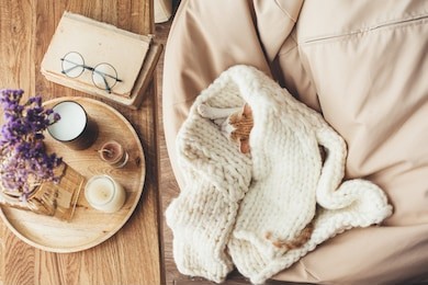 ginger kitten sleeping on knitted woolen sweater. wooden tray with home decor near the window. fall weekend cozy concept.