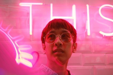 young asian hipster man in street style fashion concept and wearing sunglasses in pink neon light