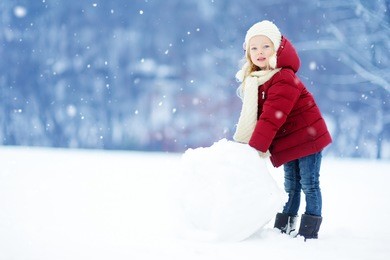 adorable little girl building a snowman in beautiful winter park. cute child playing in a snow. winter activities for kids.