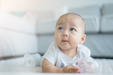adorable happy asian baby boy laughing and smiling on sofa and living room background.asian baby boy try to crawling and bite in living room.baby, people, infant and child development concept.