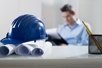 adult caucasian male architect examining documents. focus on blueprints and hardhat in foreground. horizontal shape, front view