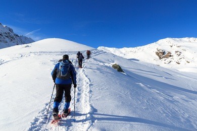group of people hiking on snowshoes and mountain snow panorama with blue sky in stubai alps, austria