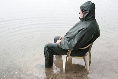 climate change, an elderly man with rain wear and rubber boots sits on a chair in the high water of the lake.
