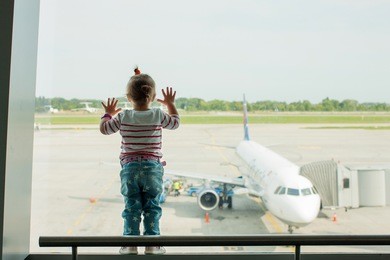 child is looking window putting his hands on the glass in  airport terminal on the plane. child travels with his parents and looks in the big window on the plane at the airport.                      