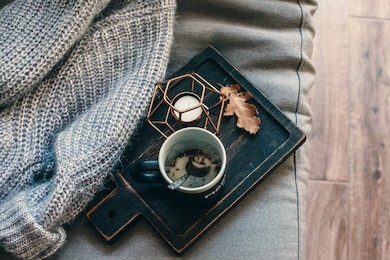 still life details of living room. a cup of coffee on the rustic wooden tray, candle and warm woolen sweater on the sofa, top view point. autumn weekend concept. fall home decoration.