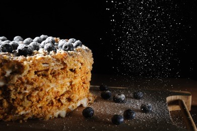 layer cake napoleon with berries blueberry on a rough wooden tray, sprinkle with powdered sugar black background for menu cafe or patisserie.