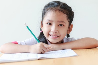 portrait of asian little girl in thai kindergarten student uniform doing homework and smiling with happiness