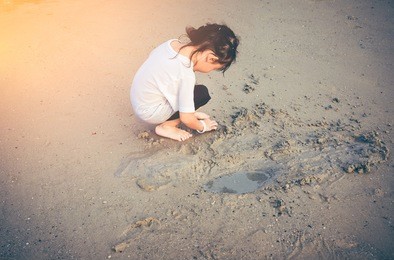 asian child playing with sand. charming young girl is looking for sea animals on the beach. outdoor at daytime with bright sunlight on summer day. concept about children are happy in nature.
