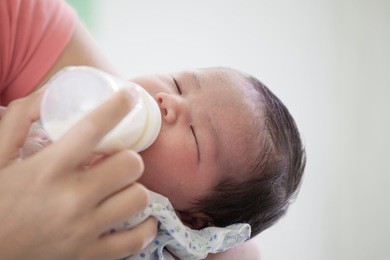 sleeping newborn baby little girl drinking a milk from bottle in her mother's arms