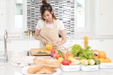 young asian female slicing paprika on cutting board at the kitchen, prepare the ingredient for cooking salad for her family