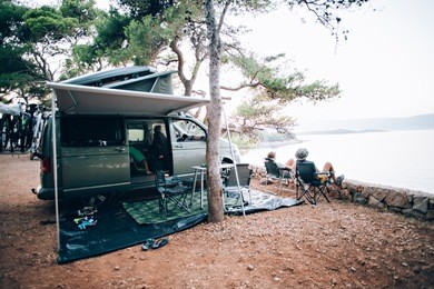 vintage film look effect photo of couple in folding chairs enjoy view of sunset over sea on camp site next to camper rv, concept family vacation, holidays and summer