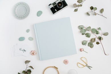 blue family or wedding photo album  with blank space for text, eucalyptus leaf, retro camera and dry rose buds on white background. flat lay, top view.