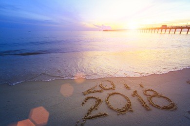 new year 2018 is coming concept - inscription 2017 and 2018 on a beach sand, the wave is starting to cover the digits 2017