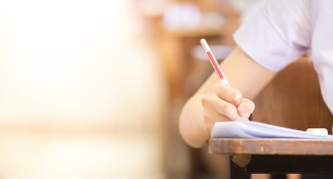 soft focus.high school or university student holding pencil writing on paper answer sheet.sitting on lecture chair taking final exam attending in examination room or classroom.student in uniform.
