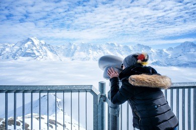 young woman tourist at the schilthorn using coin operated binocular to enjoy the magnificent panoramic view of the swiss skyline.