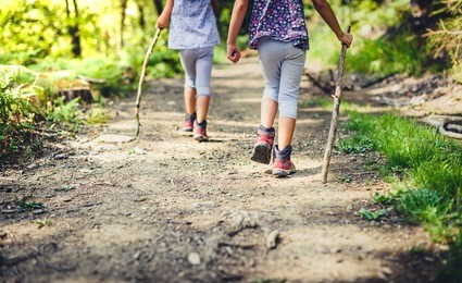 children hiking in mountains or forest with sport hiking shoes. girls are walking trough forest path wearing mountain boots and walking sticks. frog perspective with focus on the shoes.