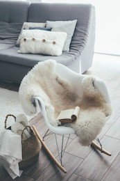 still life details of living room. sheep skin rug on modern armchair by the sofa with cushions. reading book on the rocket chair. cozy winter scene in scandinavian interior.