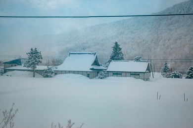 house and hut covered by snow. snow storm is coming in  winter rural landscape.  forest trees in fresh day at hokkaido, japan.