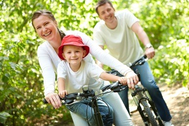 portrait of happy woman with son riding a bicycle in park on background of male