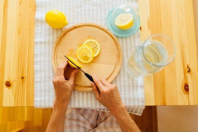 top view of woman's hands cutting lemon on the wooden board. lay flat. view from above