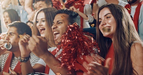 group of fans cheer for their team victory on a stadium bleachers. they wear casual fan clothes.