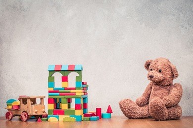 retro old toys: teddy bear, wooden house made of construction blocks and truck front concrete textured wall background. vintage instagram style filtered photography