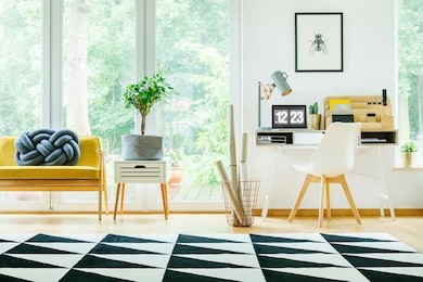 plant on cabinet next to yellow sofa with blue pillow in spacious workspace with white chair at desk