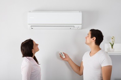 happy young couple adjusting temperature of air conditioner by remote