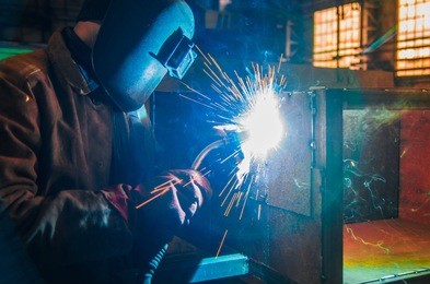 the worker in overalls and a protective mask welds metal with a welding machine. profession welder. man in protective overalls.