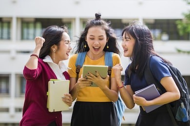 advertising, education students people knowledge concept - front view of three excited asian students receiving good news on line in tablet in an university campus.
