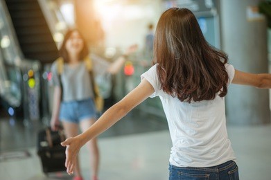 asian girl picking up her friend at airport's arrival gate, welcomes back home from studying or working abroad. young couple love and hug, or traveling concept