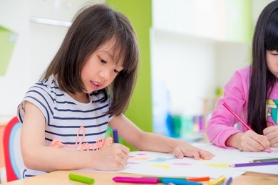 preschool girl kid drawing with color pencil on white paper on table in classroom with friends and teacher,kindergarten education concept