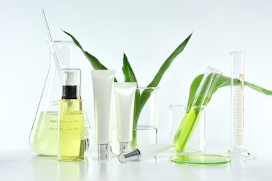 cosmetic bottle containers with green herbal leaves and scientific glassware, blank label package for branding mock-up, research and develop natural organic beauty skincare product concept.