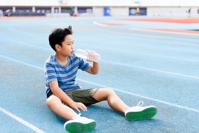 young asian thai boy drinking water from bottle during resting on the blue track after running